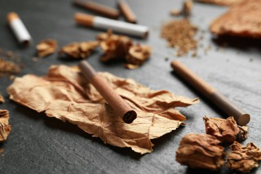 Kurumuş tütün yaprakları ve sigaralar siyah masada, yakın plan.