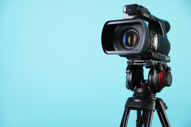 Açık mavi arkaplanda tripodu olan modern video kamera, metin için boşluk