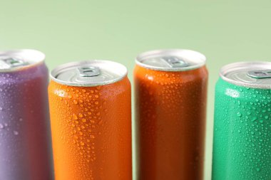 Soluk yeşil arka planda renkli alüminyum içecek kutuları, yakın plan