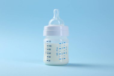 Açık mavi arka planda sütle beslenme şişesi