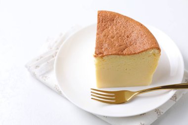 Piece of tasty Japanese Castella sponge cake and fork on white table, closeup