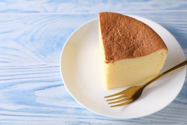Piece of tasty Japanese Castella sponge cake and fork on light blue wooden table, closeup. Space for text