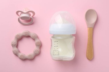 Pembe arka planda süt, kaşık, emzik ve iplikle beslenme şişesi, düz yatıyordu.