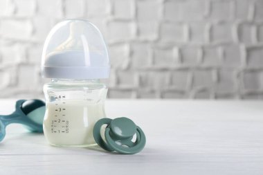 Süt, emzik ve bebek çıngırağı ile beslenme şişesi beyaz ahşap masa üzerinde, metin için boşluk