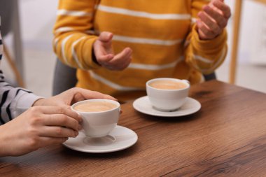 Kahve molası. Ahşap masada elinde sıcak içecekler olan kadınlar, yakın plan.