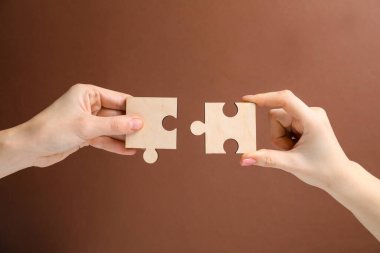 İş stratejisi ve takım çalışması konsepti. Ortaklar yapboz parçalarını kahverengi arkaplanda birleştiriyor, yakın plan