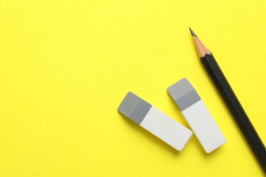 Erasers and pencil on yellow background, top view. Space for text