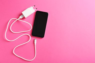 USB power adapter with charge cable and smartphone on pink background, flat lay. Space for text