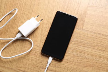 USB güç adaptörü, ahşap masadaki akıllı telefona bağlı şarj kablosu, üst görünüm