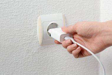 Kadın USB güç adaptörünü şarj kablosuyla kapalı mekandaki elektrik prizine takıyor.