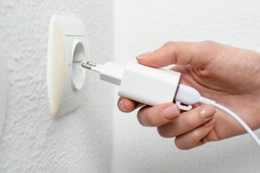 Kadın USB güç adaptörünü şarj kablosuyla kapalı mekandaki elektrik prizine takıyor.