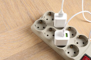 USB adapters with charge cables in power strip on wooden table, above view. Space for text