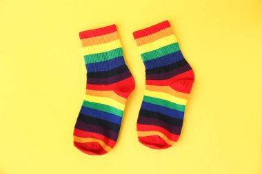 Pair of socks in LGBT colors on yellow background, flat lay