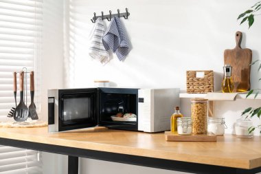 Mikrodalga fırını aç, mutfak gereçleri ve mutfak aletleri içeride, ahşap masada.