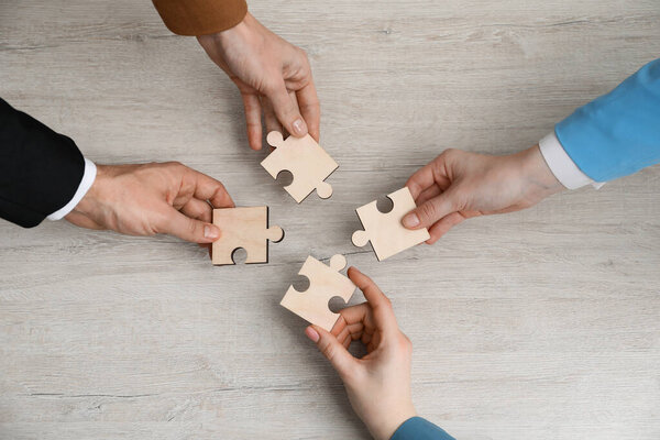 Teamwork. Group of people putting puzzle pieces together at wooden table, top view