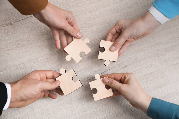 Teamwork. Group of people putting puzzle pieces together at wooden table, top view