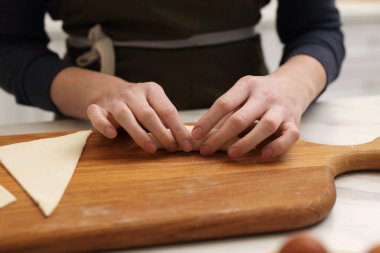 Aydınlık masada taze hamurdan kruvasan yuvarlayan kadın, yakın plan.