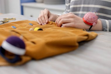 İçerideki aydınlık masada kumaşla çalışan kadın, yakın plan.