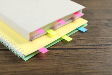 Book and notebook with colorful tabs on wooden table, closeup