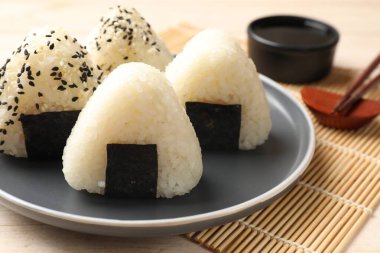 Rice balls (onigiri), soy sauce and chopsticks on wooden table, closeup. Traditional Japanese dish