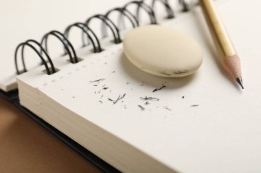 Eraser, pencil, scraps and notebook on brown background, closeup