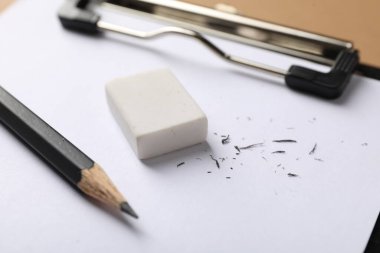 Kahverengi arkaplanda silgi, kalem, kırıntı ve pano, yakın plan