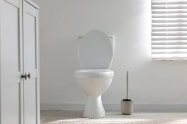 Toilet and brush near white wall in bathroom
