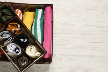 Organizers with folded clothes on wooden table, top view. Space for text