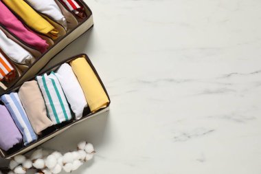 Organizers with folded clothes and cotton branch on white marble table, flat lay. Space for text