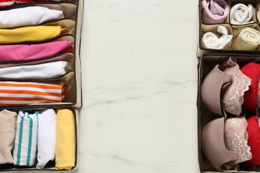 Organizers with folded clothes and underwear on white marble table, flat lay. Space for text