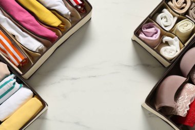 Organizers with folded clothes and underwear on white marble table, flat lay. Space for text