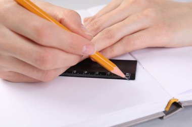 Beyaz masadaki deftere cetvel ve kalemle çizim yapan kadın, yakın plan.