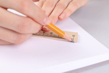 Beyaz masadaki deftere cetvel ve kalemle çizim yapan kadın, yakın plan.