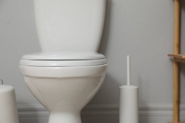 Ceramic toilet bowl and brush near grey wall indoors