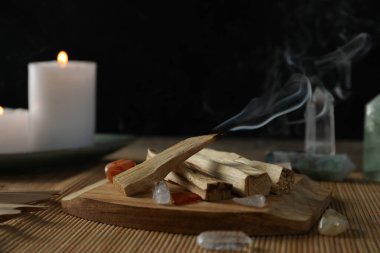 Smoldering palo santo stick, gemstones and burning candles on table, closeup