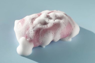 Soap bar with foam on grayish blue background, closeup
