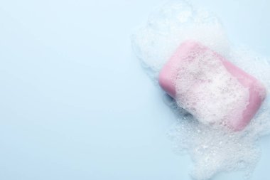 Açık mavi arka planda köpüklü sabun çubuğu, üst manzara. Metin için boşluk