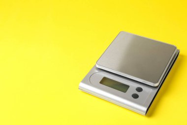 Modern electronic kitchen scale on yellow background, closeup. Space for text