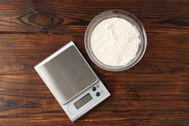 Electronic kitchen scale and bowl with flour on wooden table, flat lay