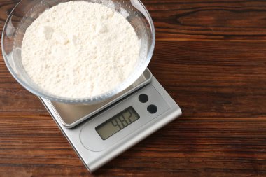 Electronic kitchen scale with bowl of flour on wooden table, above view. Space for text