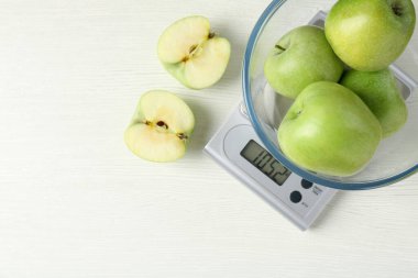 Electronic kitchen scale with bowl of green apples on white wooden table, flat lay. Space for text