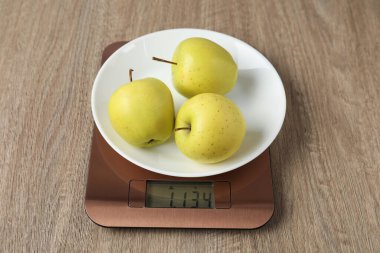 Modern electronic kitchen scale with apples on wooden table, closeup