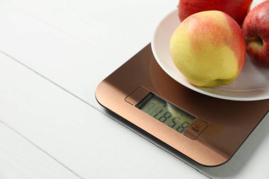 Modern electronic kitchen scale with apples on white wooden table, closeup. Space for text