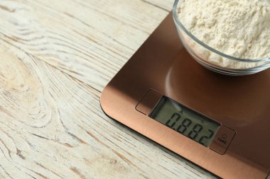 Modern electronic kitchen scale with bowl of flour on wooden table, closeup. Space for text