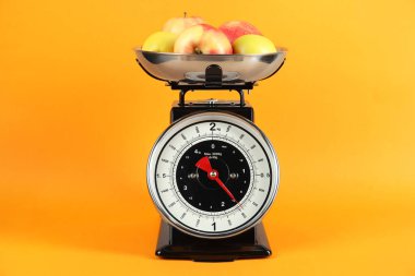Mechanical kitchen scale with bowl of apples on yellow background