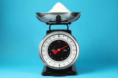 Mechanical kitchen scale with bowl of flour on blue background