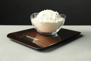 Electronic kitchen scale with bowl of flour on grey textured table against black background, closeup