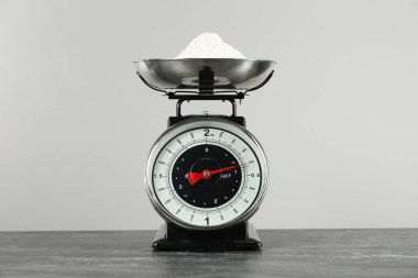 Mechanical kitchen scale with bowl of flour on dark textured table against grey background