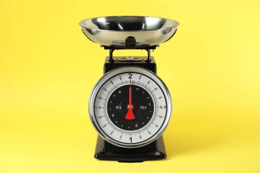 Mechanical kitchen scale with bowl on yellow background, closeup