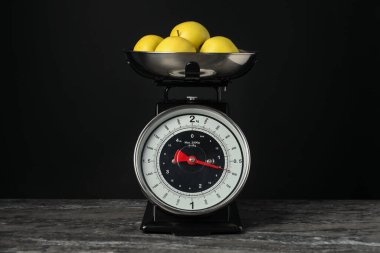 Mechanical kitchen scale with bowl of apples on dark textured table against black background